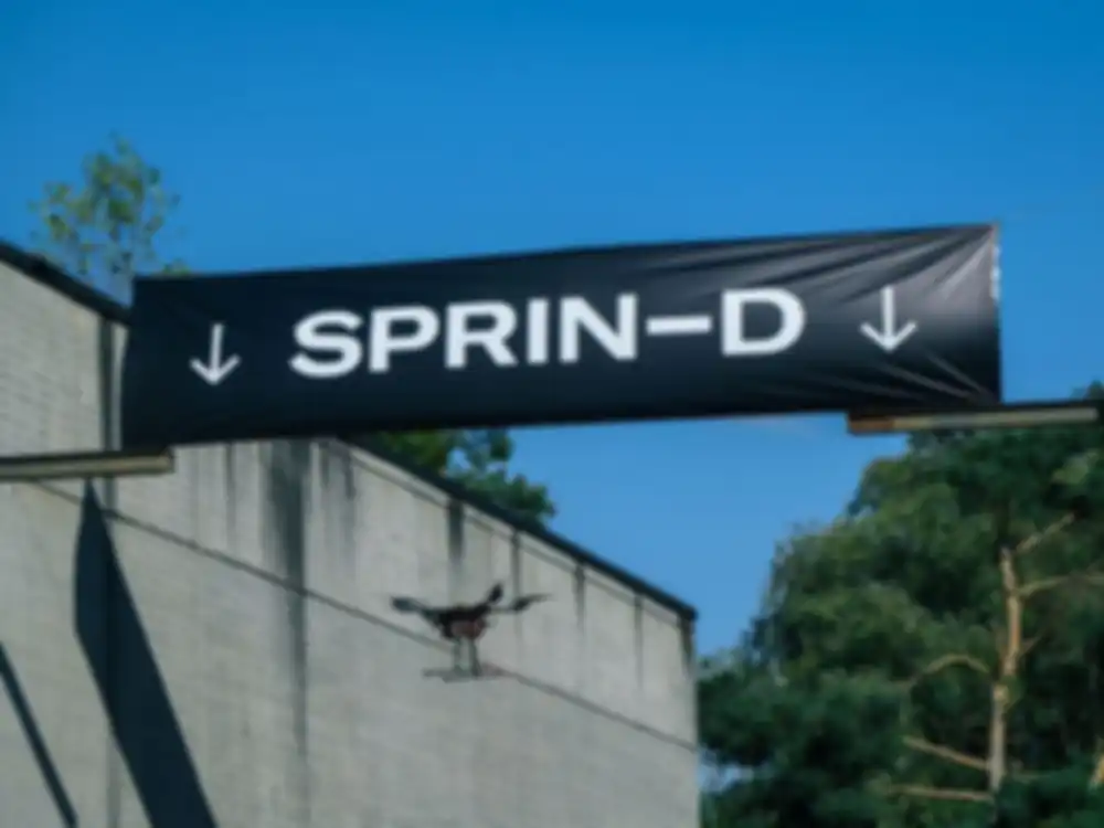 Eine Drone fliegt autonom zwicschen zwei Hangars und unter einem Banner hindurch mit der Aufschrift SPRIND