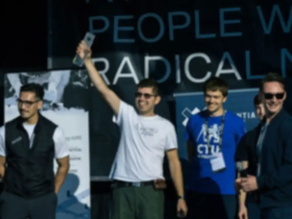 The winning team stands on stage and holds a trophy in the air