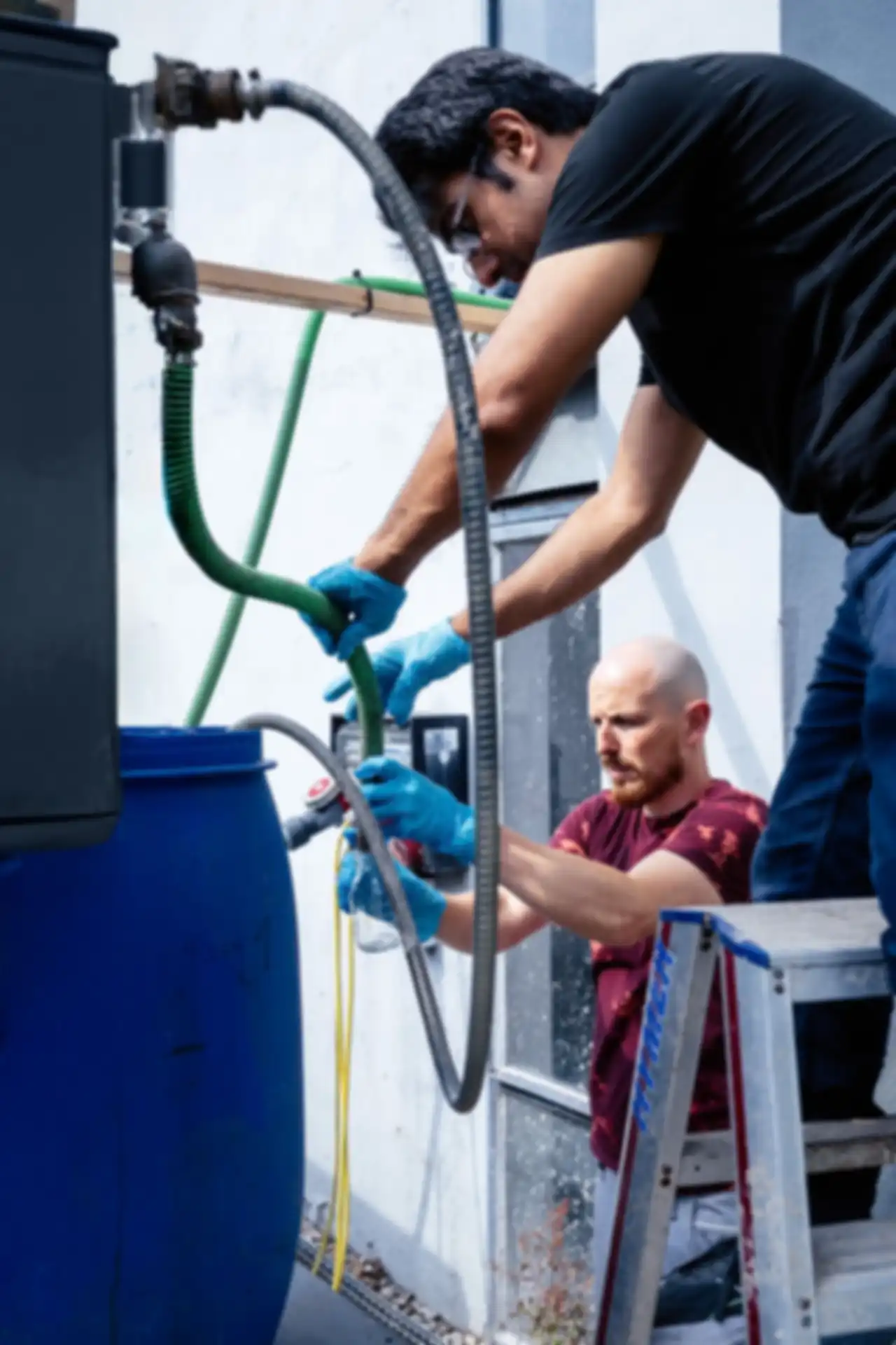 Zwei Männer arbeiten an einer Anlage mit Fässern und Schläuchen