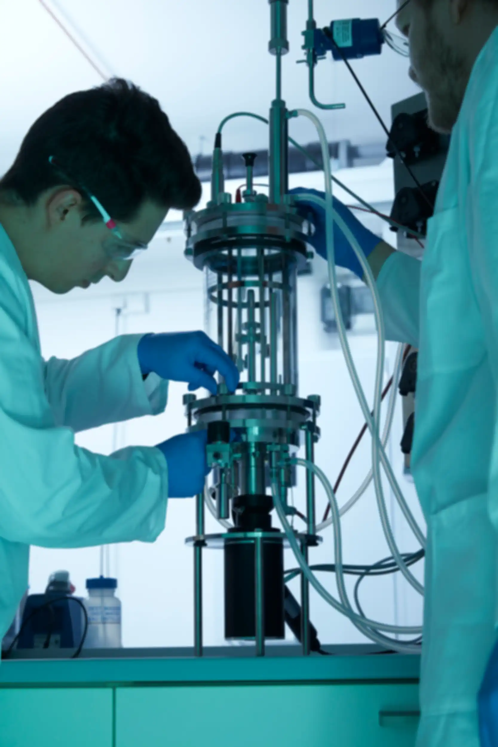 Two men wearing lab coats and safety goggles preparing a piece of technical equipment