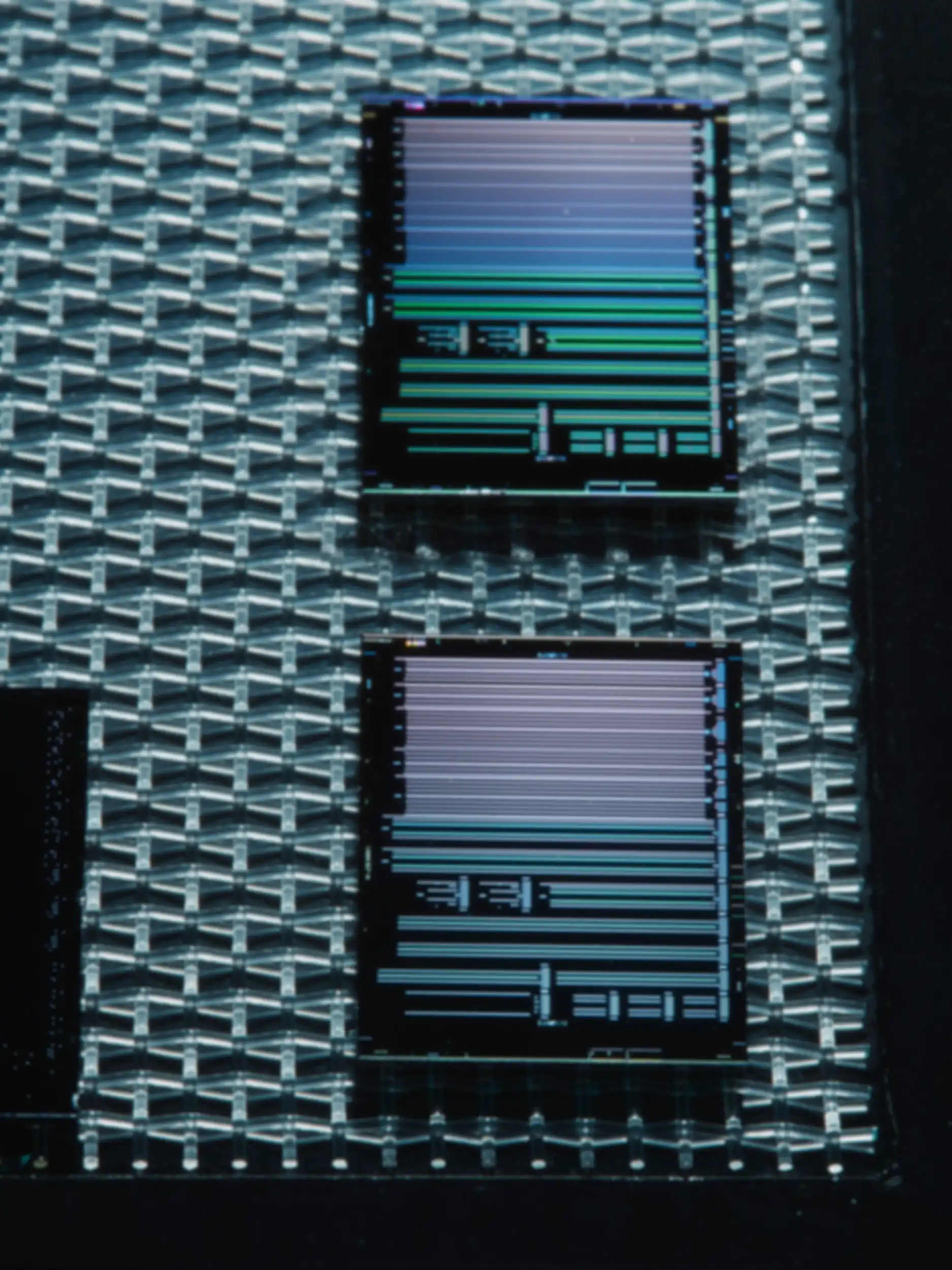 Two rectangular microchips with fine, horizontal line patterns rest on a textured surface