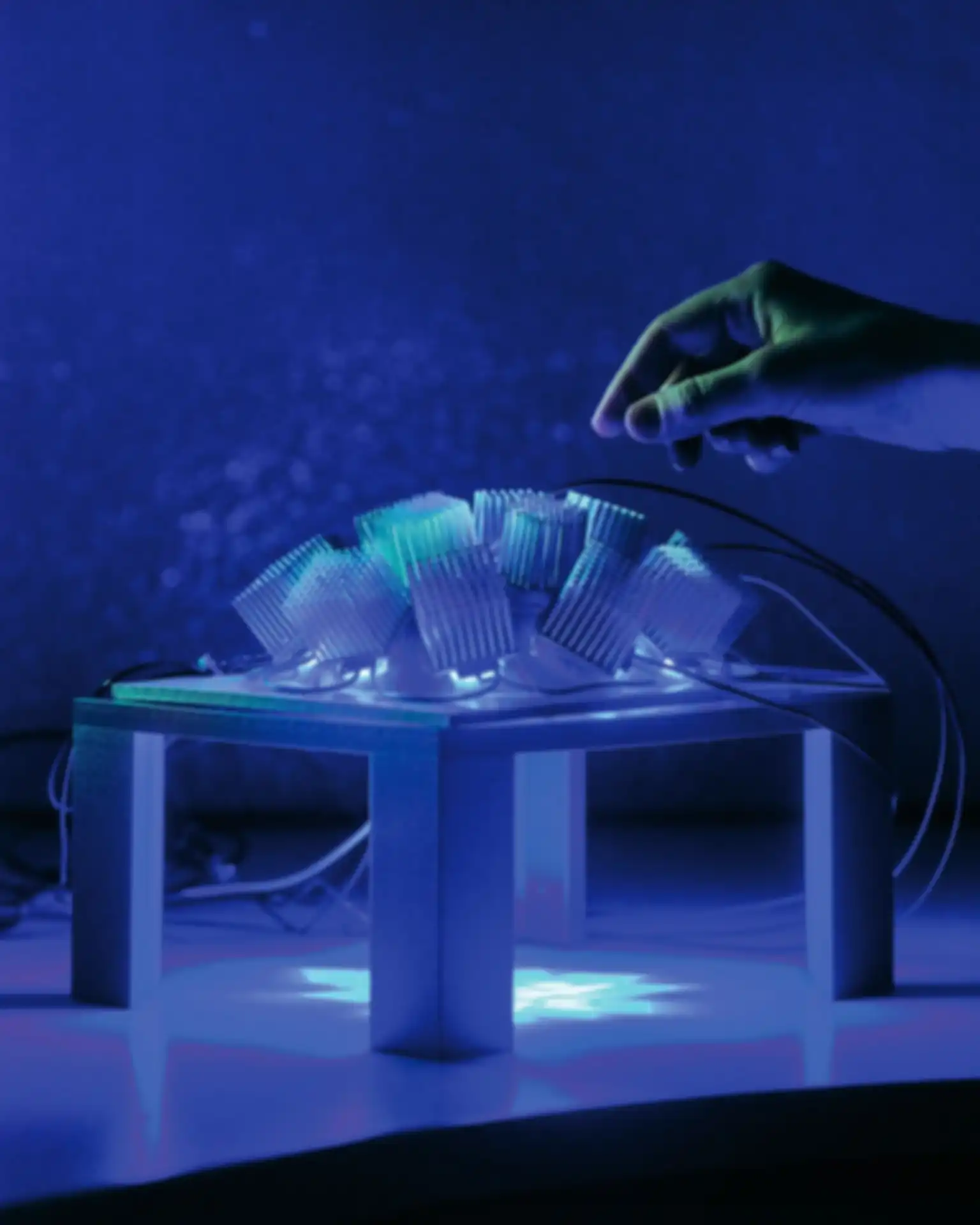 Eine Hand schwebt über einer rechteckigen Plattform mit mehreren Bauteilen in blauem Licht