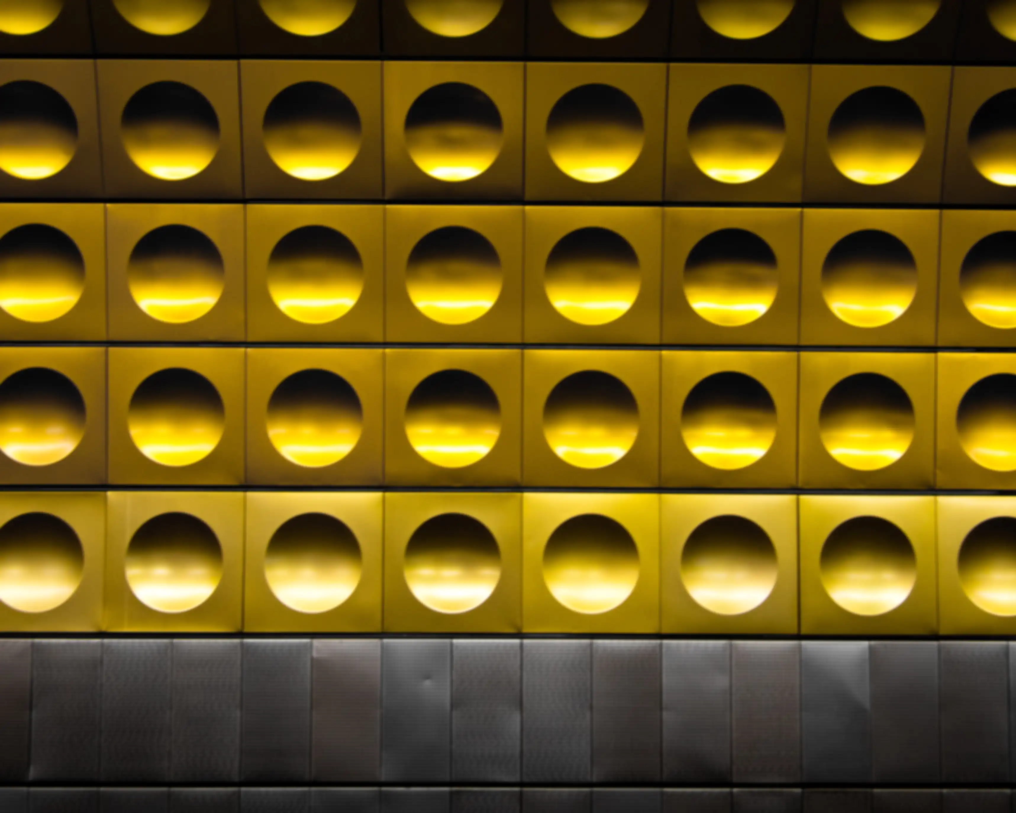 Gelbe, kreisförmige Lichtöffnungen in einer geometrischen Wandstruktur