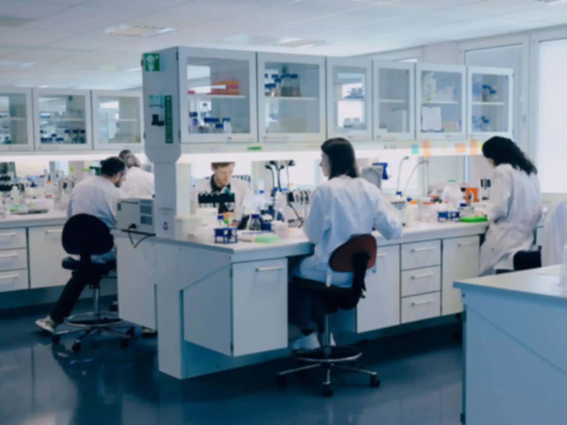 Five people in white lab coats are sitting in a lab and working