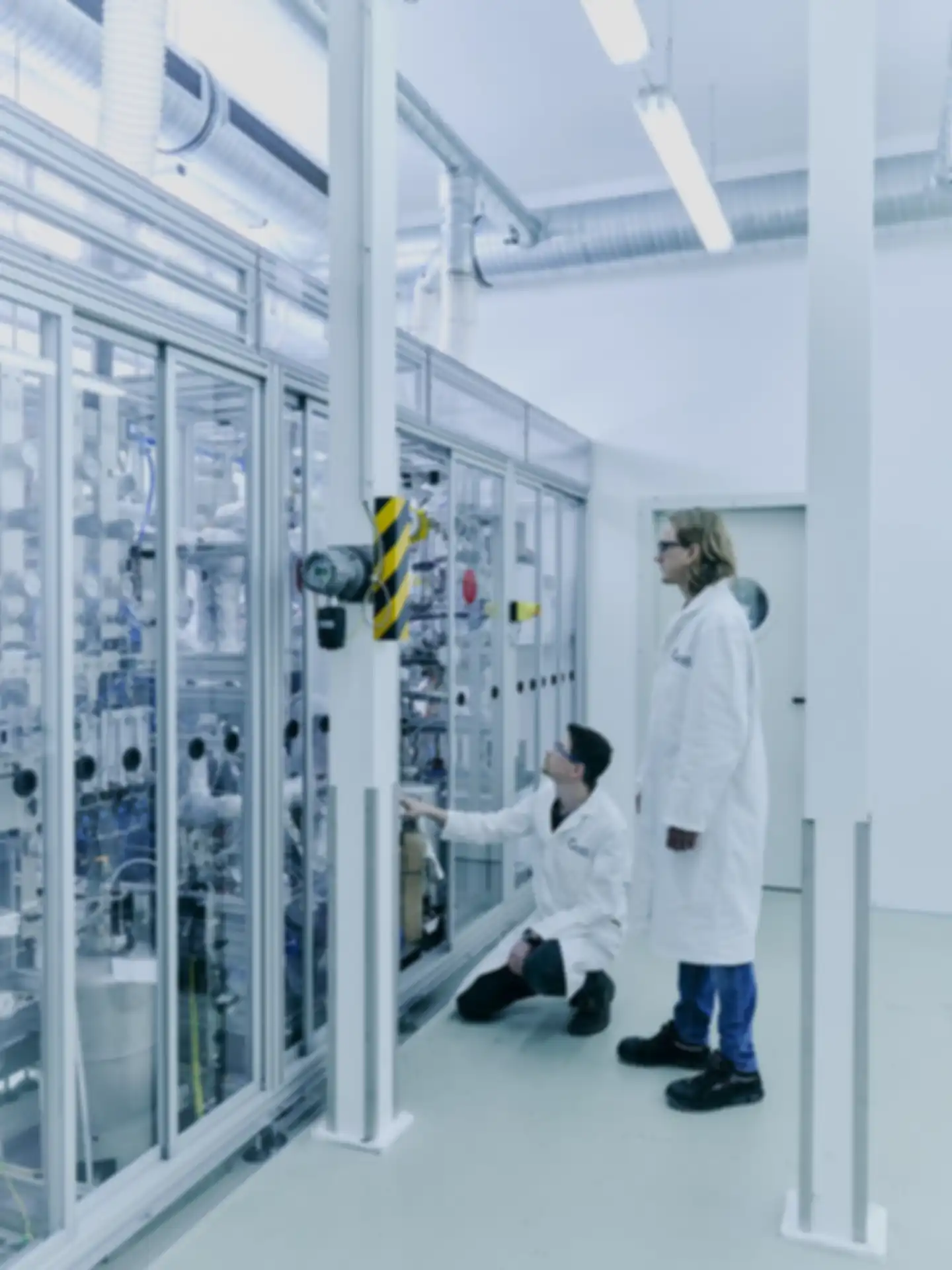 Two men in white lab coats standing in front of a large piece of laboratory equipment