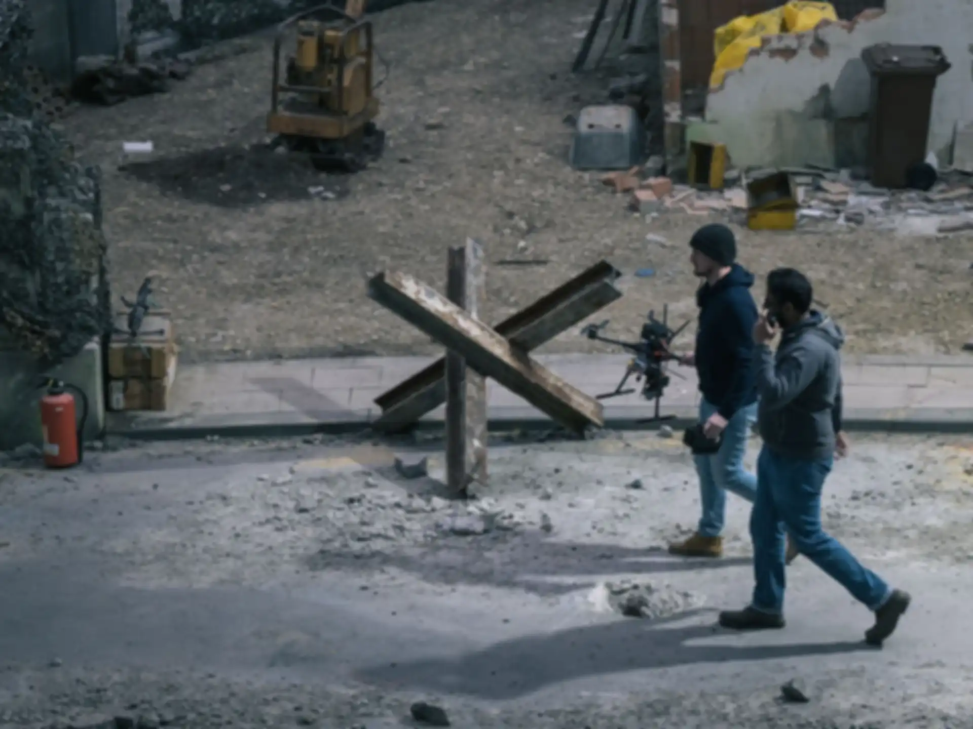 Two people are walking across the test site. One of them is carrying a drone