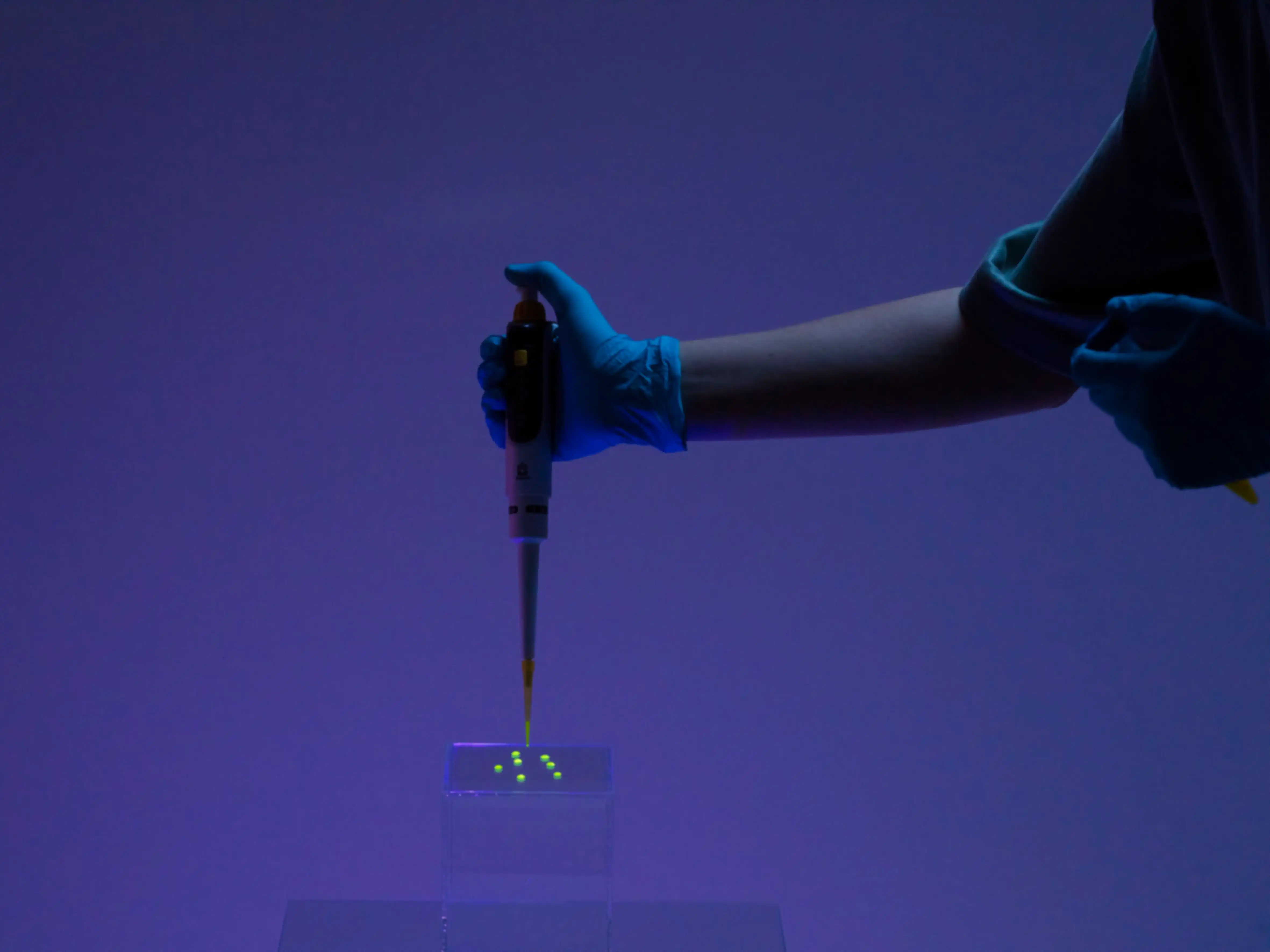 Eine Person tröpfelt eine gelbe Flüssigkeit auf einen Glaswürfel, mit einer Pipette