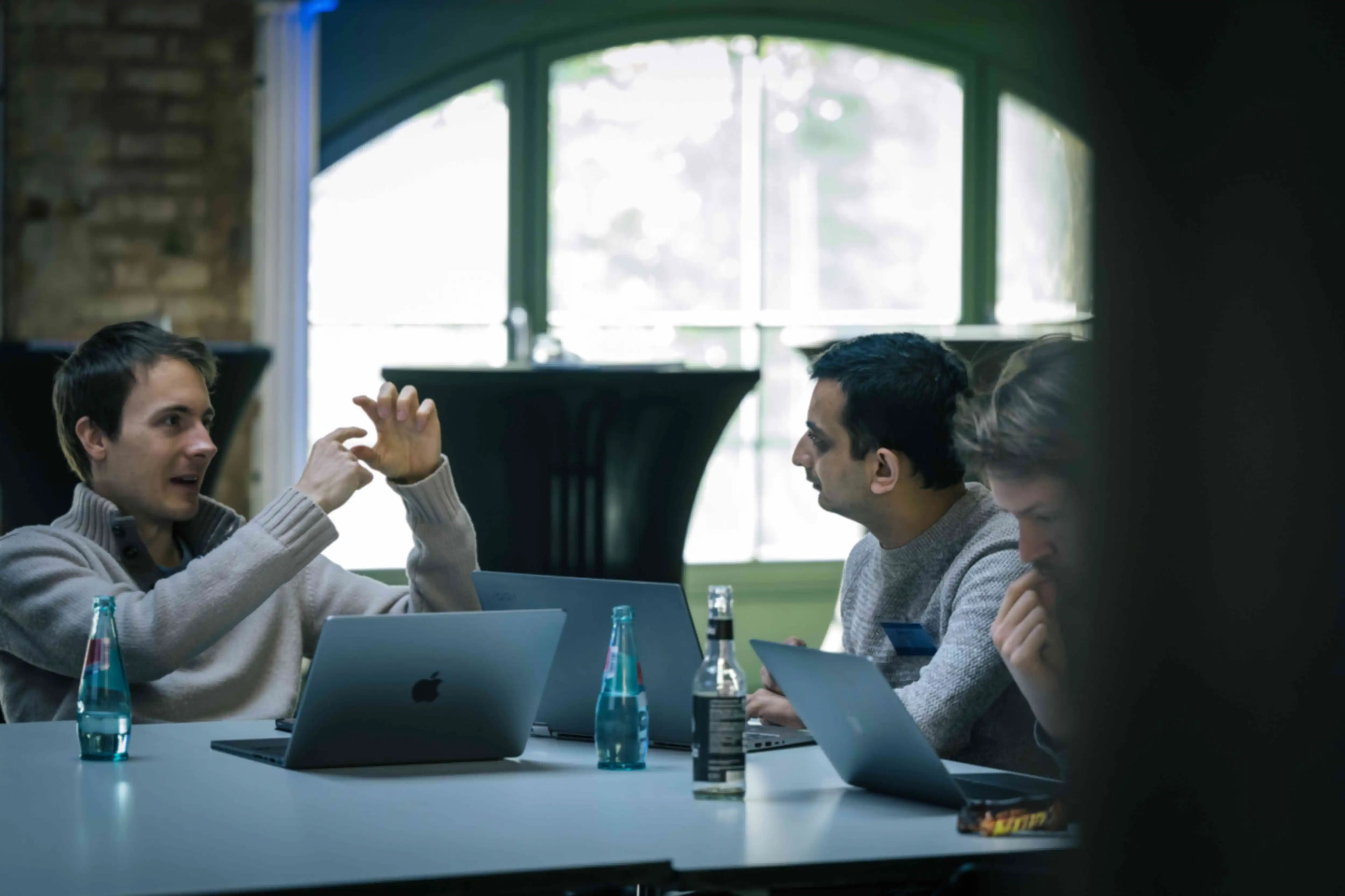 Two people talking at a table. Their laptops are in front of them.
