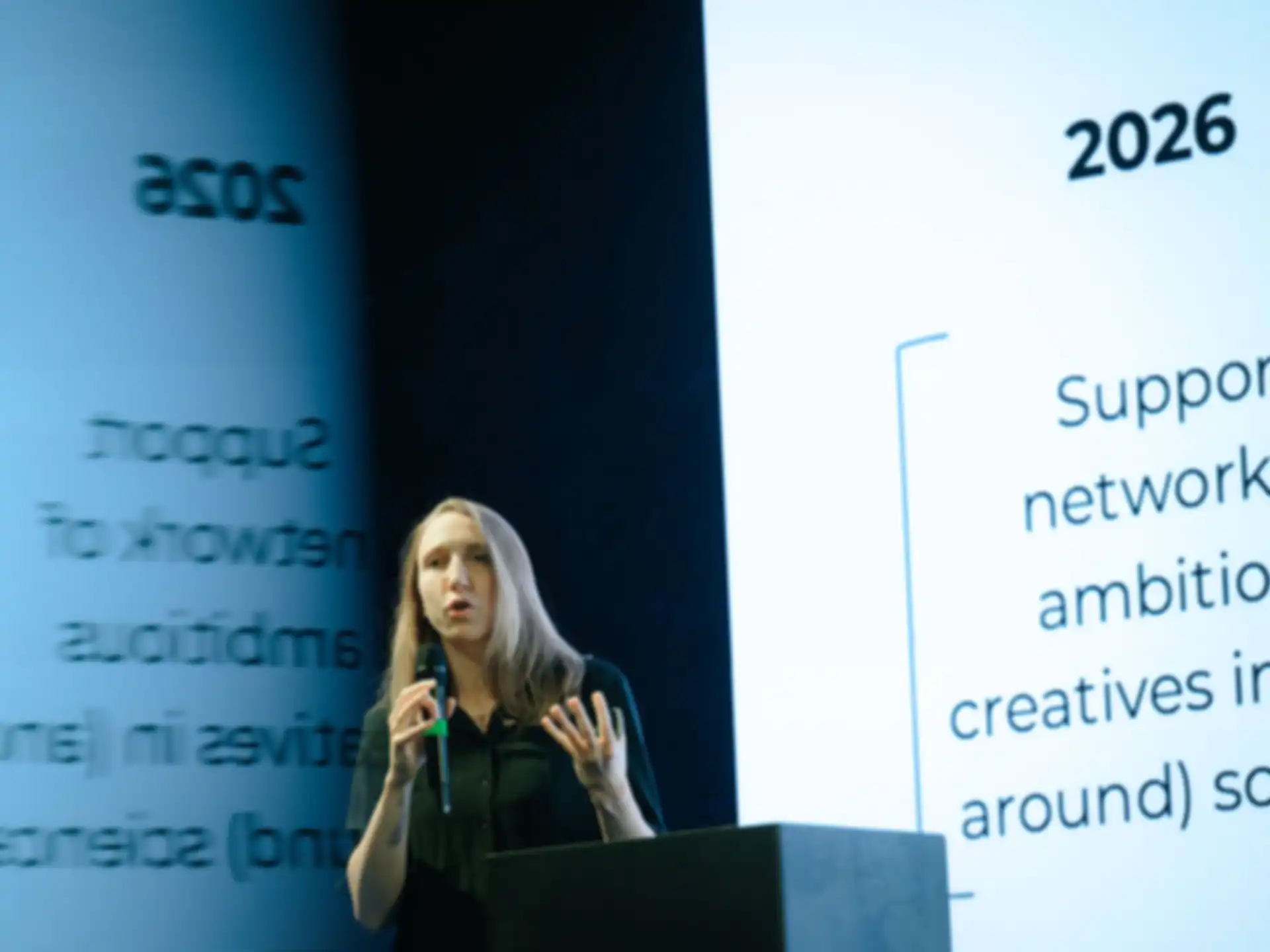 A speaker on stage. Behind her is a screen