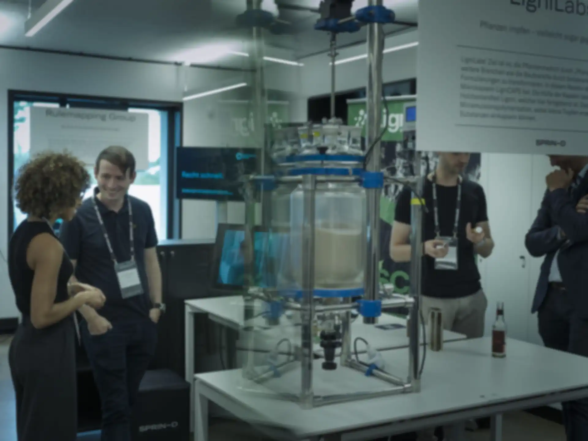 Mehrere Personen unterhalten sich auf der Messe. Mittig von ihnen befindet sich eine technologische Apparatur