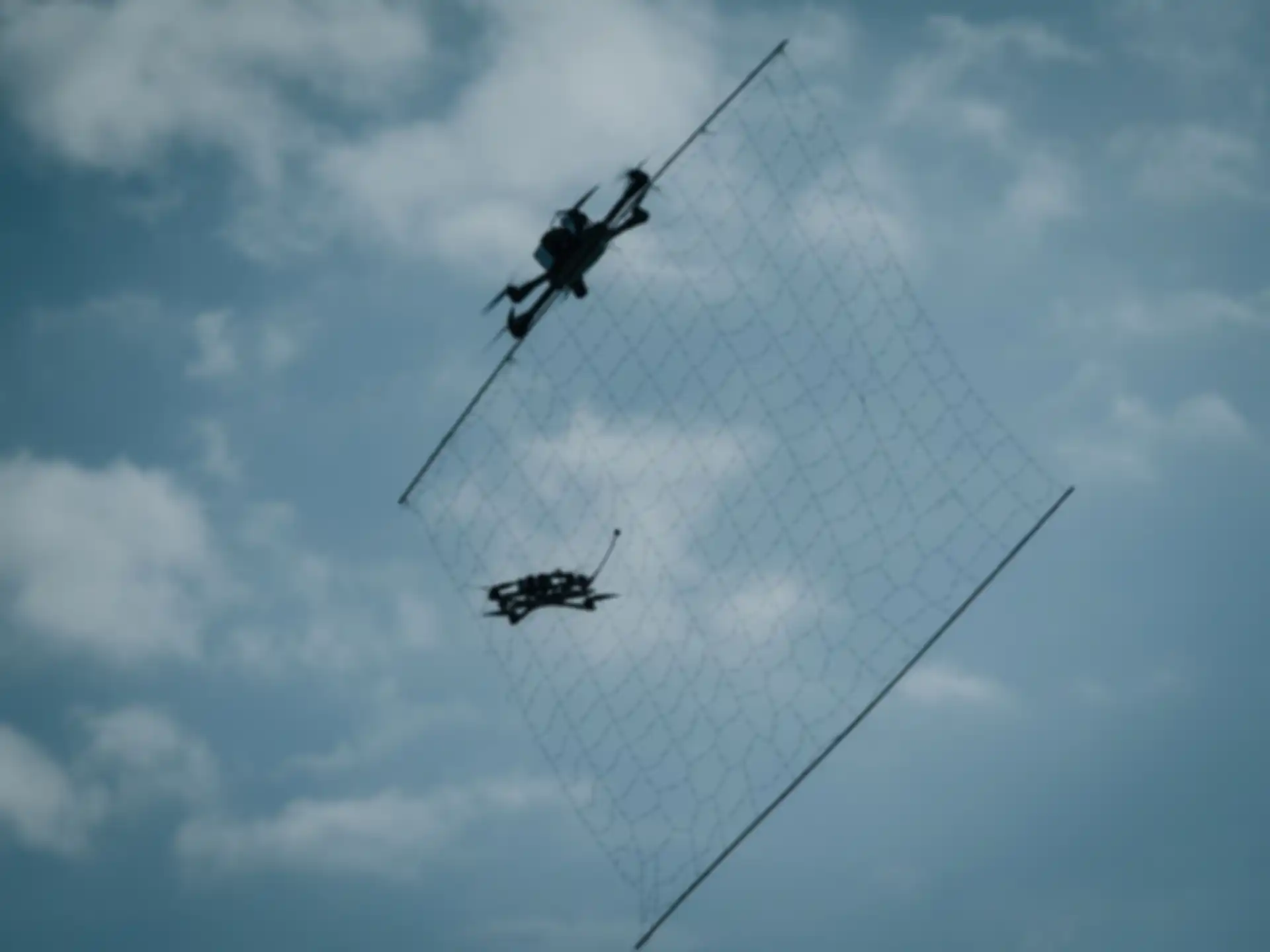Zwei Dronen in der Luft. Die eine Drone wirft ein Netz auf die andere