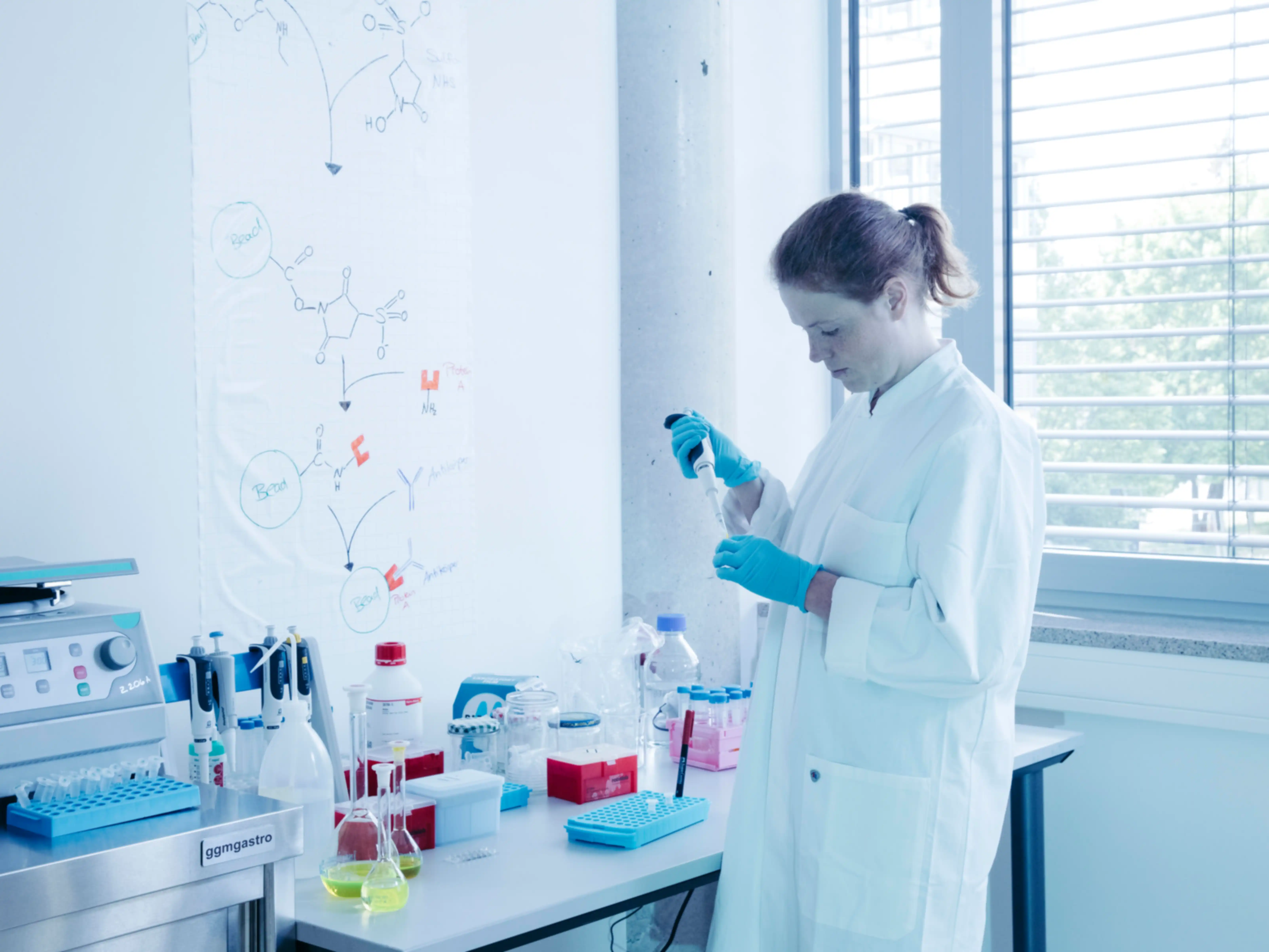 Eine Frau mit Laborkittel befüllt ein Behältnis mit einer Pipette in einer Laborumgebung