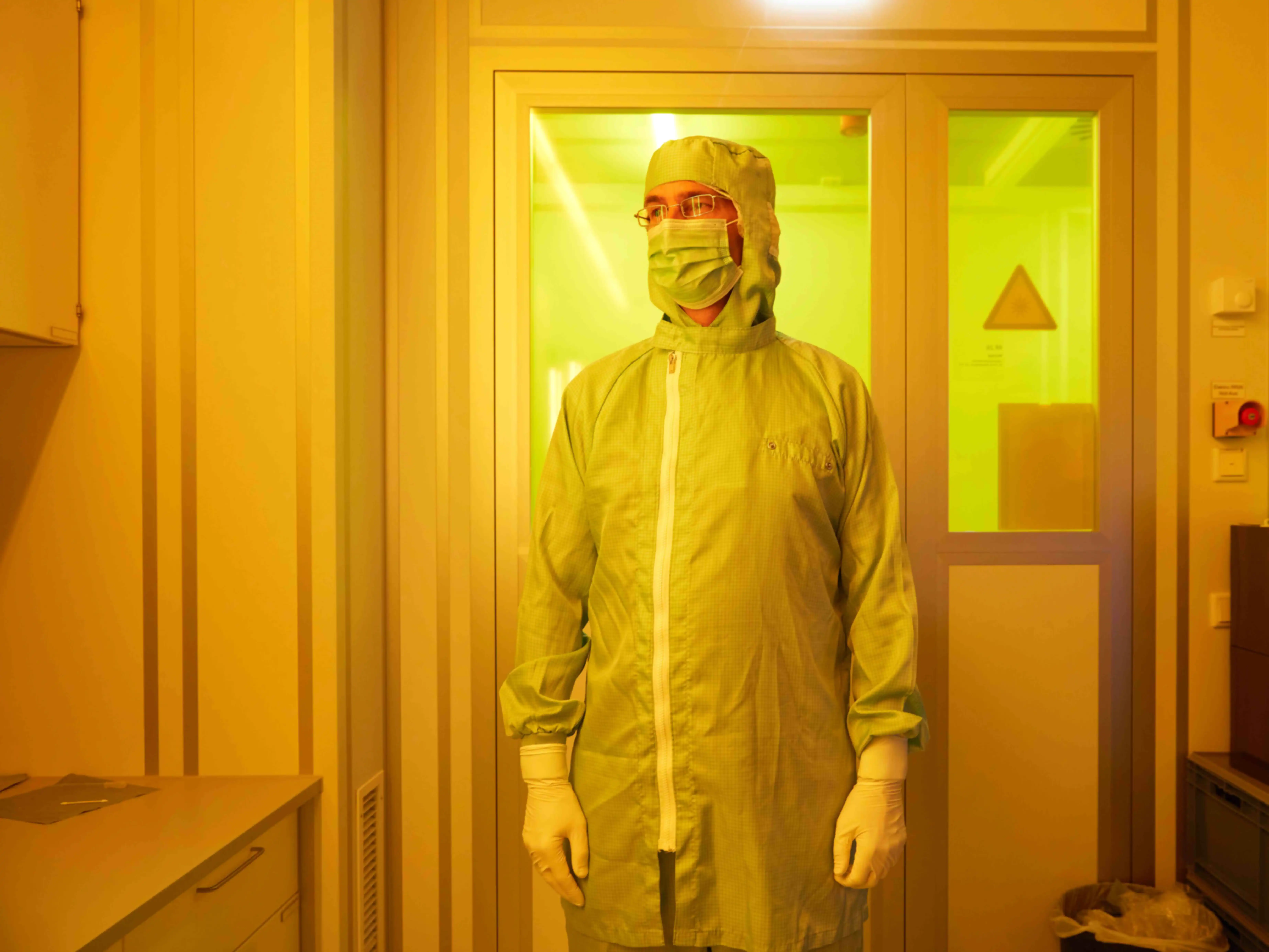 Portrait eines Labormitarbeiters mit Ganzkörperschutz, Mundschutz und Plastikhandschuhen