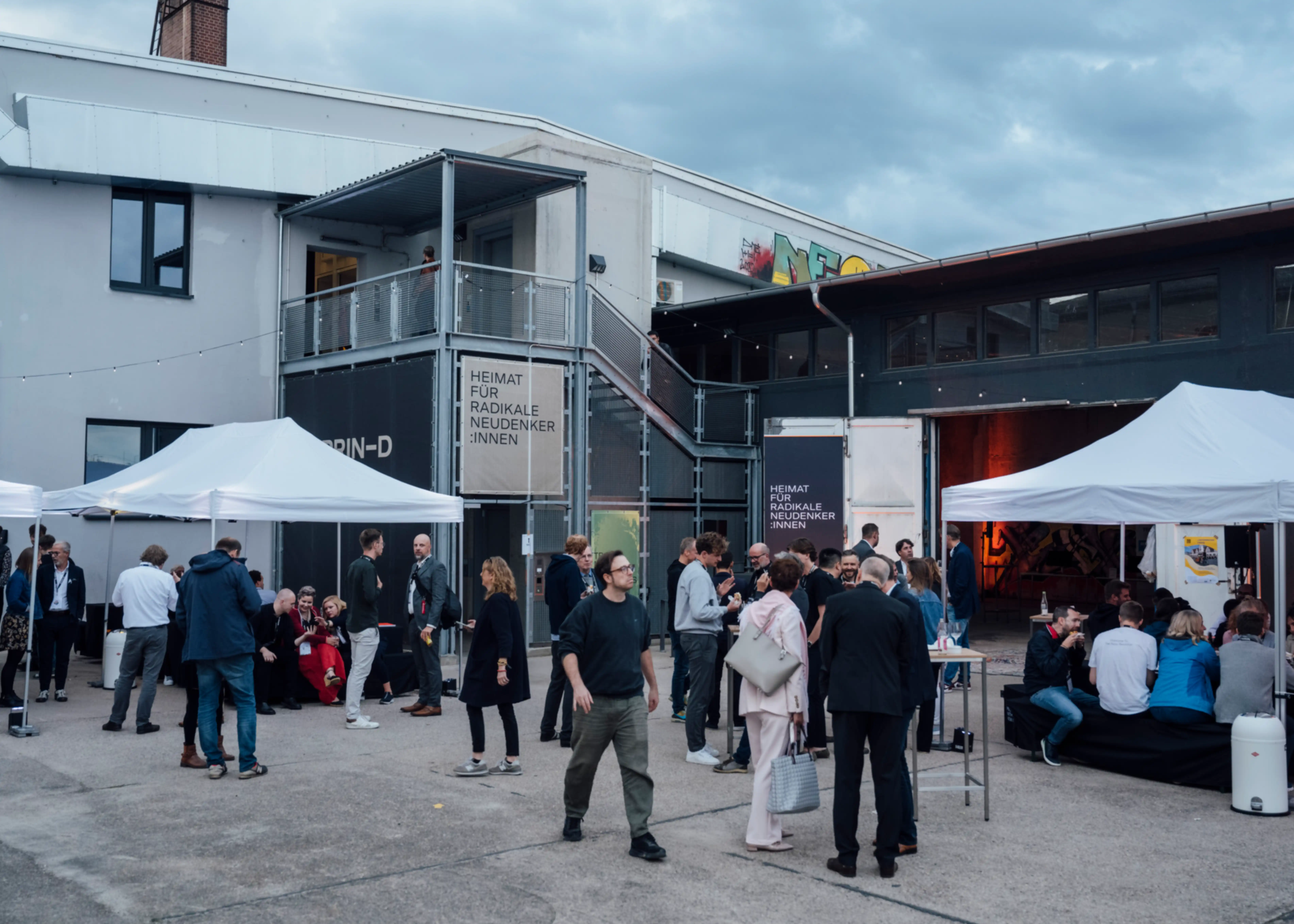The outdoor area of the farm festival. Some people are chatting, while others are walking around.
