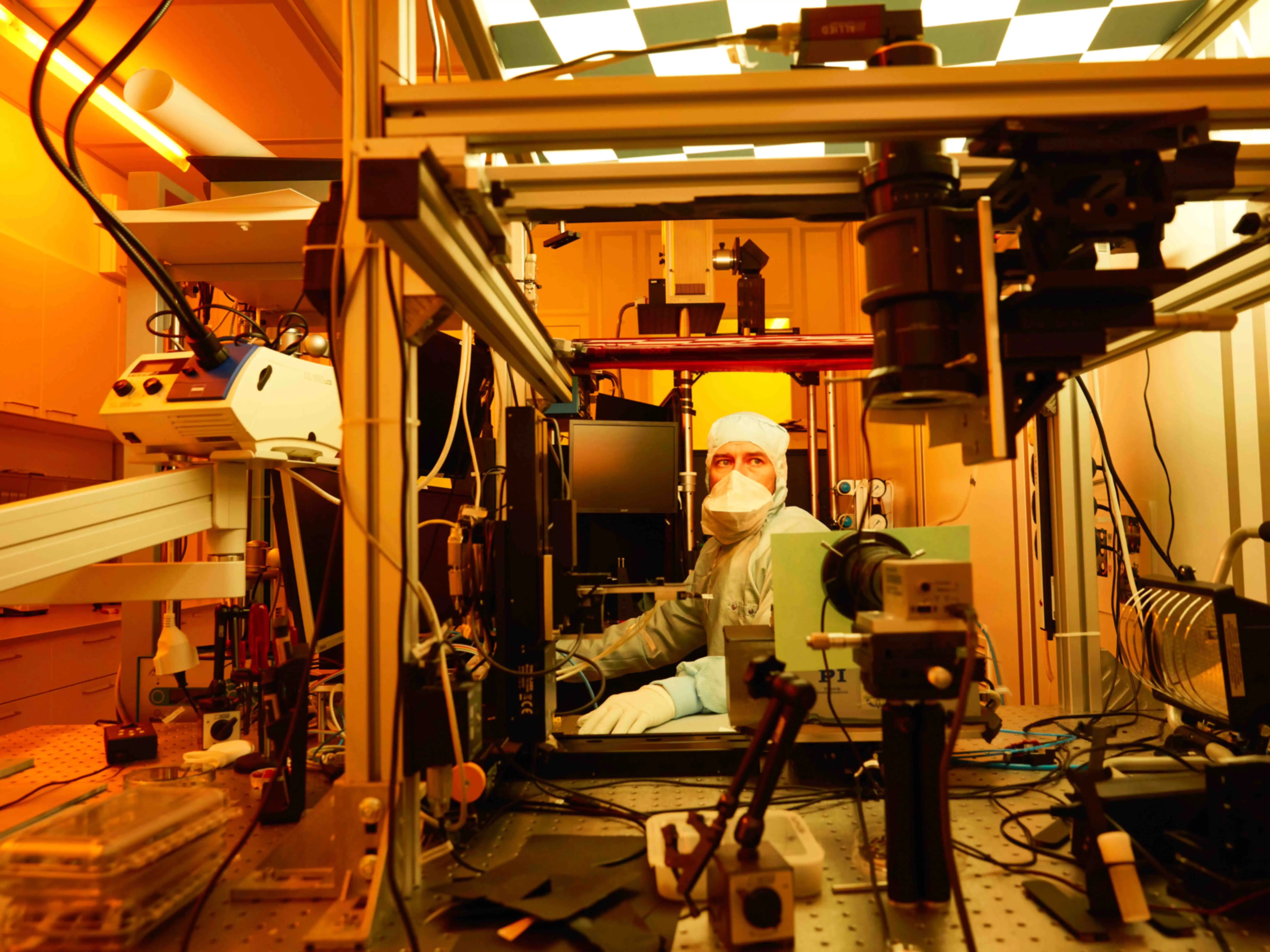 Ein Labormitarbeiter mit Ganzkörperschutz und Mundschutz zwischen einigen technischen Apparaturen