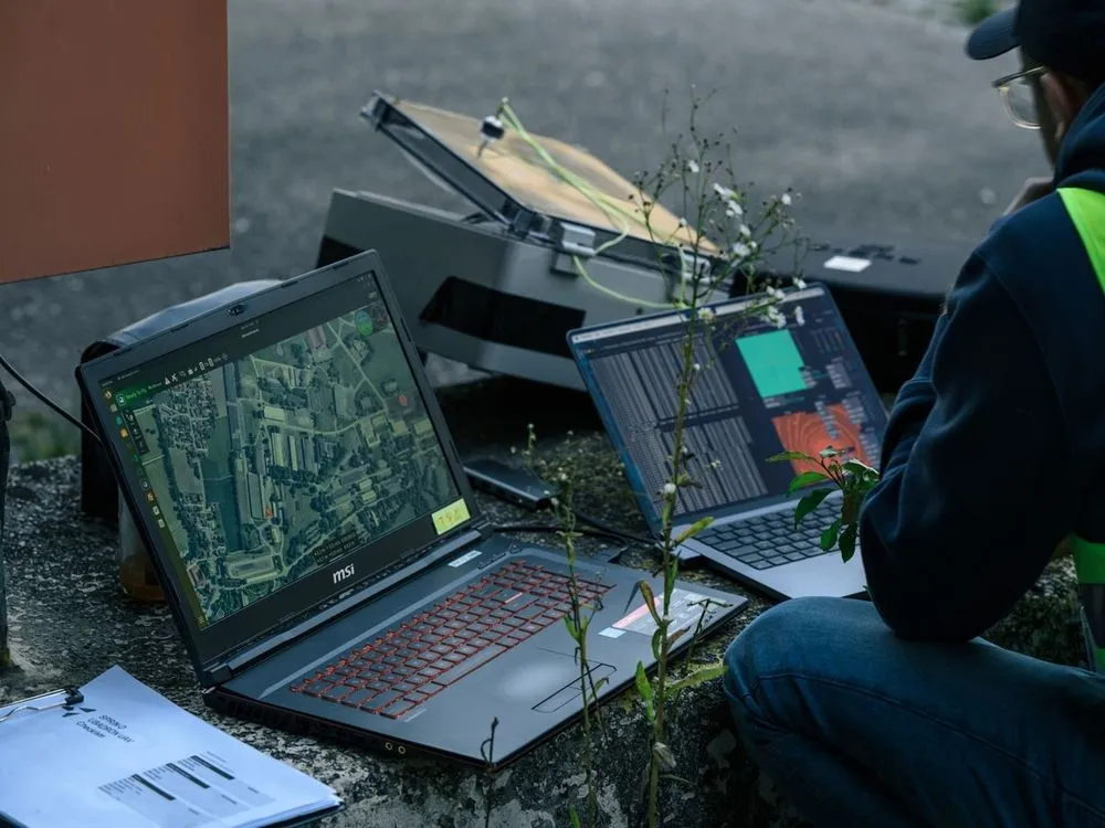 Eine Person arbeitet auf dem Flugplatz mit Laptops und mehreren Geräten um die Drohnen zu steuern.