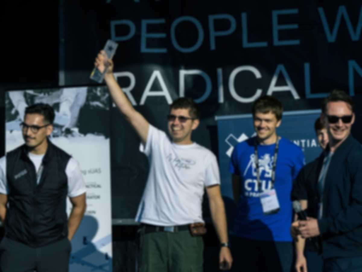 The winning team stands on stage and holds a trophy in the air