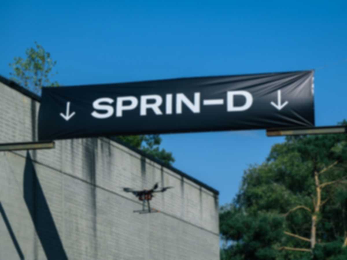 A drone flies autonomously between two hangars and under a banner with the inscription SPRIND